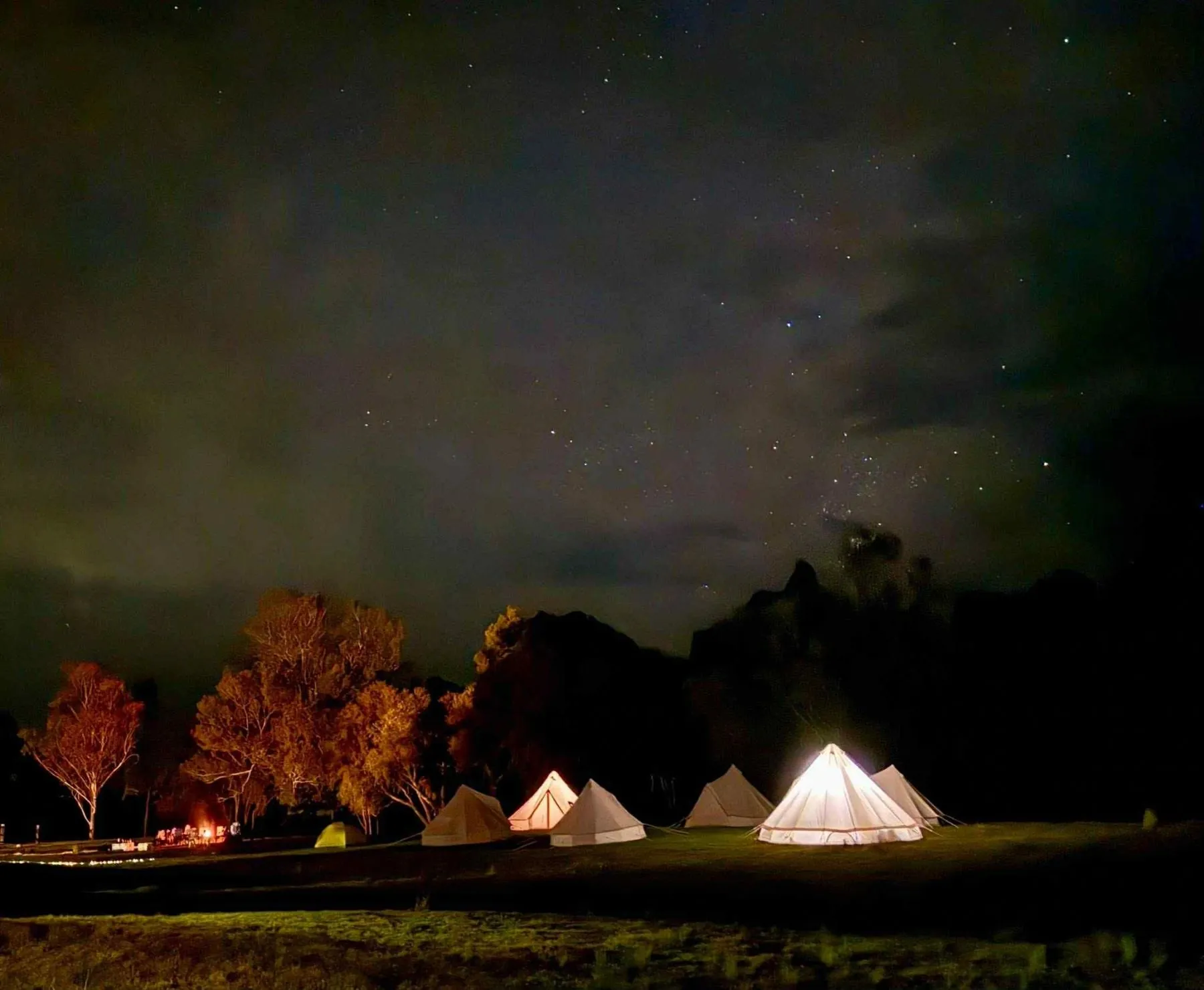 Bell tents glowing at night under a starry sky